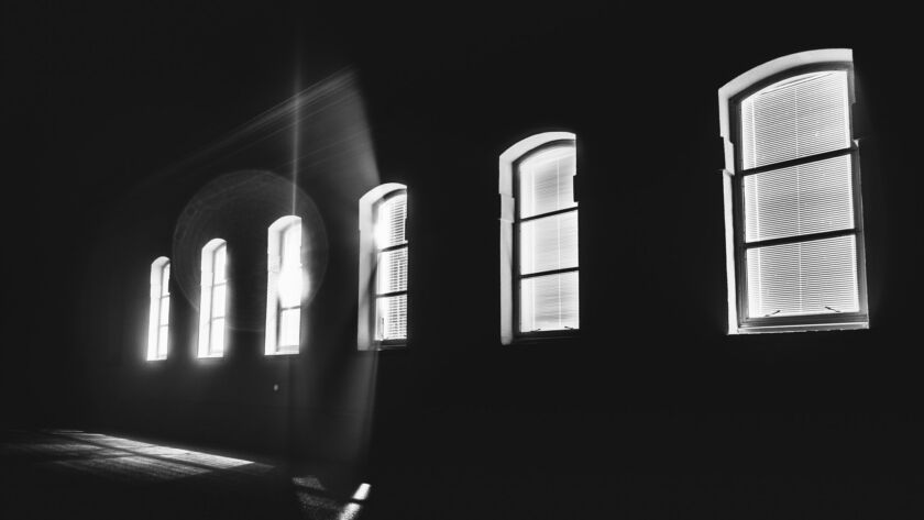 Bright light shinning through a row of windows in the middle of the night; black and white