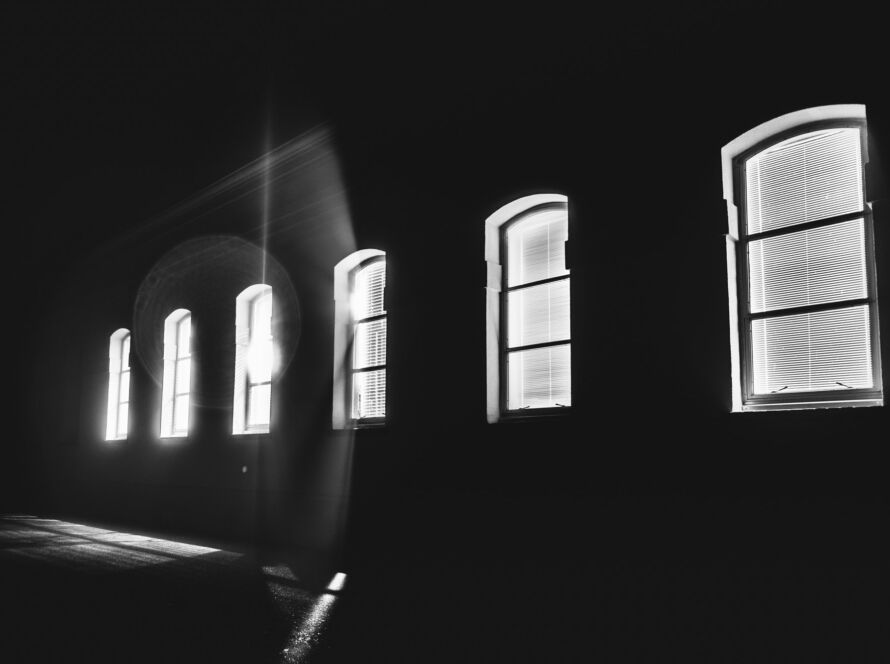 Bright light shinning through a row of windows in the middle of the night; black and white