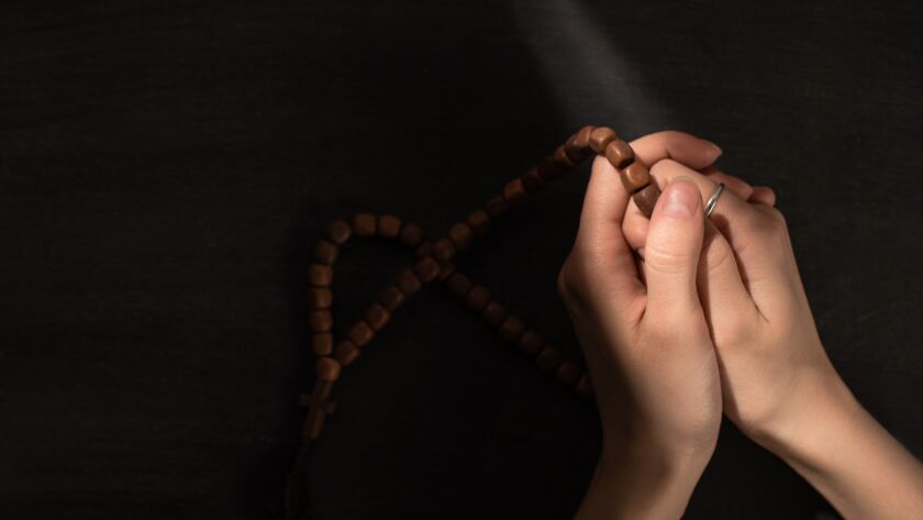 cropped view of woman praying with rosary on dark background