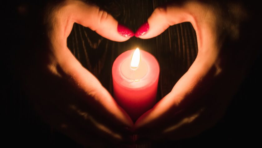 Female hands folded in the shape of a heart and a candle flame in the dark