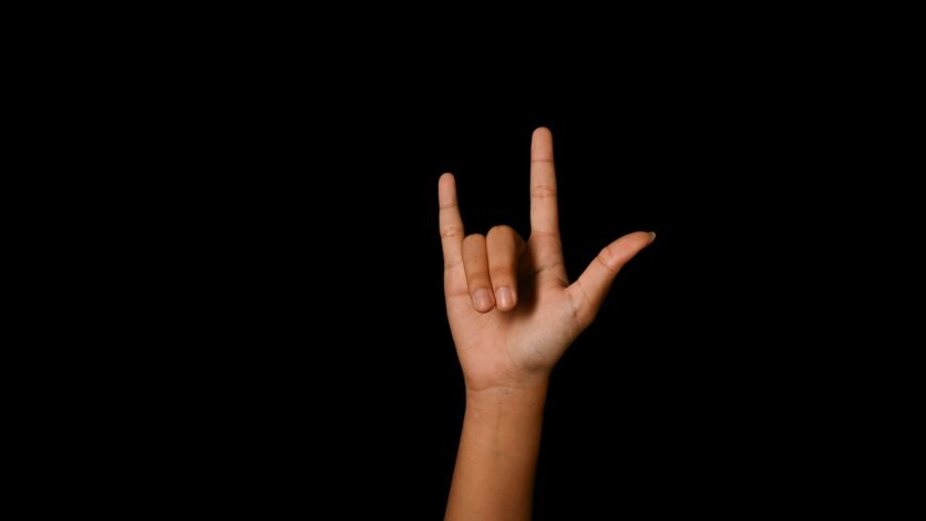 Hand showing I LOVE YOU in American sign language on black background.