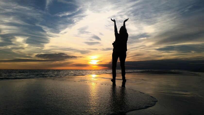Silhouetted babyboomer on beach at golden hour giving thanks for beautiful sky at night in dark.
