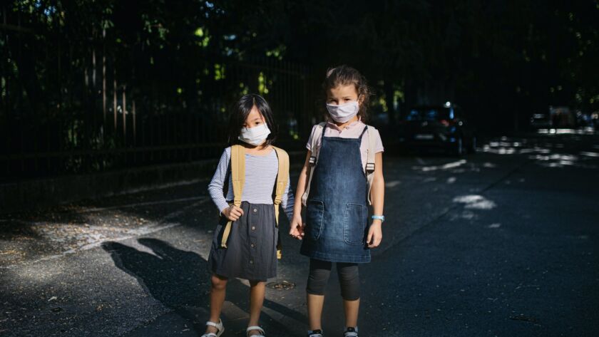 Small school girls with face mask outdoors in town, coronavirus concept.